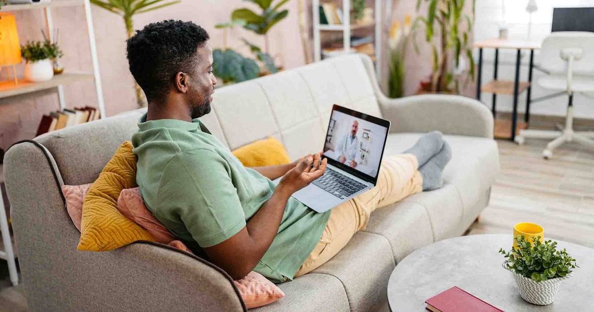 Person sitting on a couch while having a telehealth appointment Person sitting on a couch while having a telehealth appointment