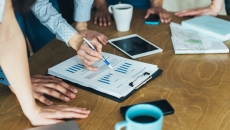 People standing around a table looking at a document People standing around a table looking at a document