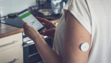 A patient with a wearable sensor patch checking their blood glucose level through a mobile app