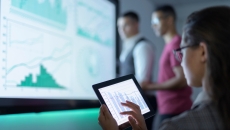 Three people in a room looking at number charts Three people in a room looking at number charts