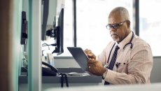 A doctor using a tablet in a patient exam room A doctor using a tablet in a patient exam room