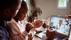 A father and daughter talking to a doctor through a video chat on a laptop.