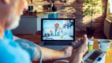 An older man talking with a provider on his laptop while checking his blood pressure