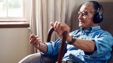 An older man wearing headphones checking his smartphone