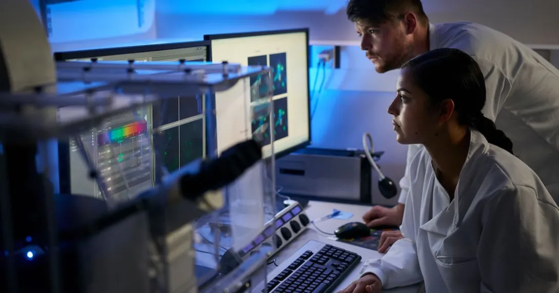 Two healthcare professionals, one sitting down and one standing up, looking at computer screens in a dark room Two healthcare professionals, one sitting down and one standing up, looking at computer screens in a dark room