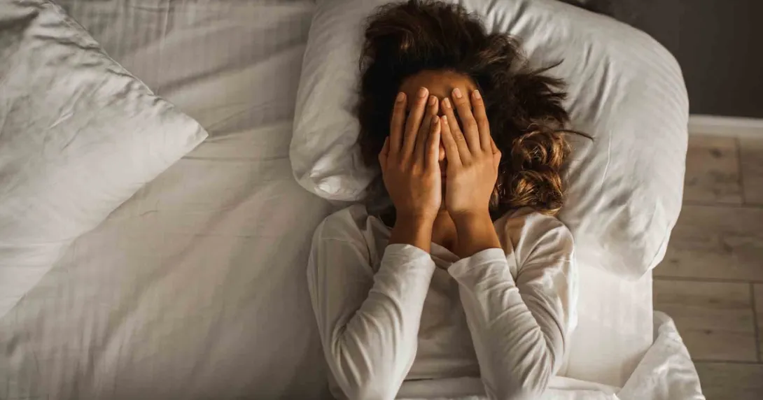 Person lying in bed with their hands over their eyes Person lying in bed with their hands over their eyes