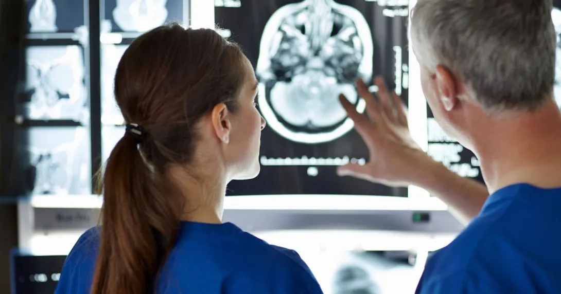 Two healthcare providers looking at a diagnostic image of a brain scan Two healthcare providers looking at a diagnostic image of a brain scan