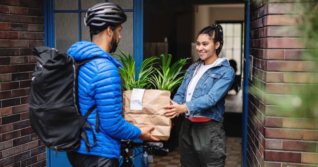 Food delivery person handing a bag to a person standing in their doorway