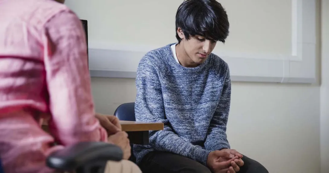 Two people sitting in a room, one with their head down
