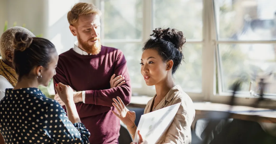 People standing in a circle with one of them holding a large piece of paper