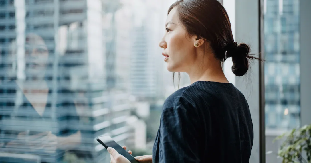 Person standing up while holding a phone and looking out a window