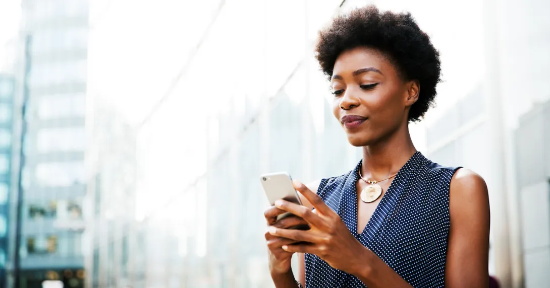 Person standing outside while looking at a phone with the appearance of a city behind her