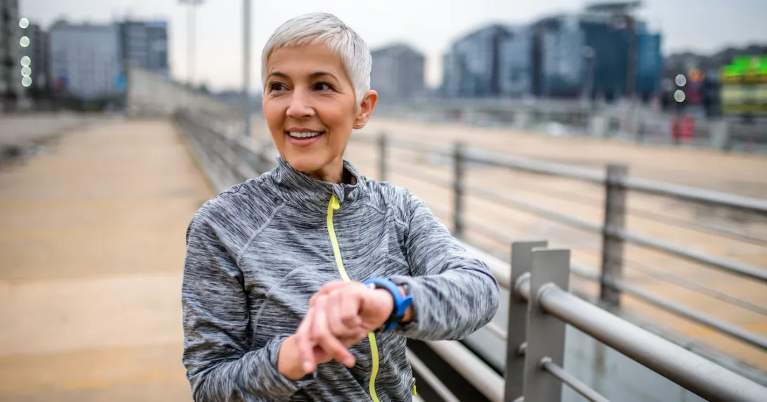 Person standing on a boardwalk while holding their wrist with a smartwatch on it