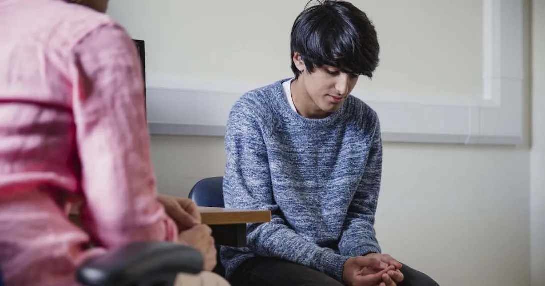 Two people sitting in a room, one with their head down