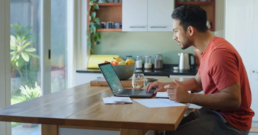Person sitting at a table in a kitchen looking at their laptop
