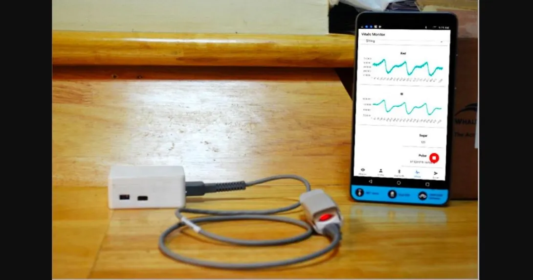 Amrita Spandanam featuring a finger clip and a mobile app showing vital parameter measurements