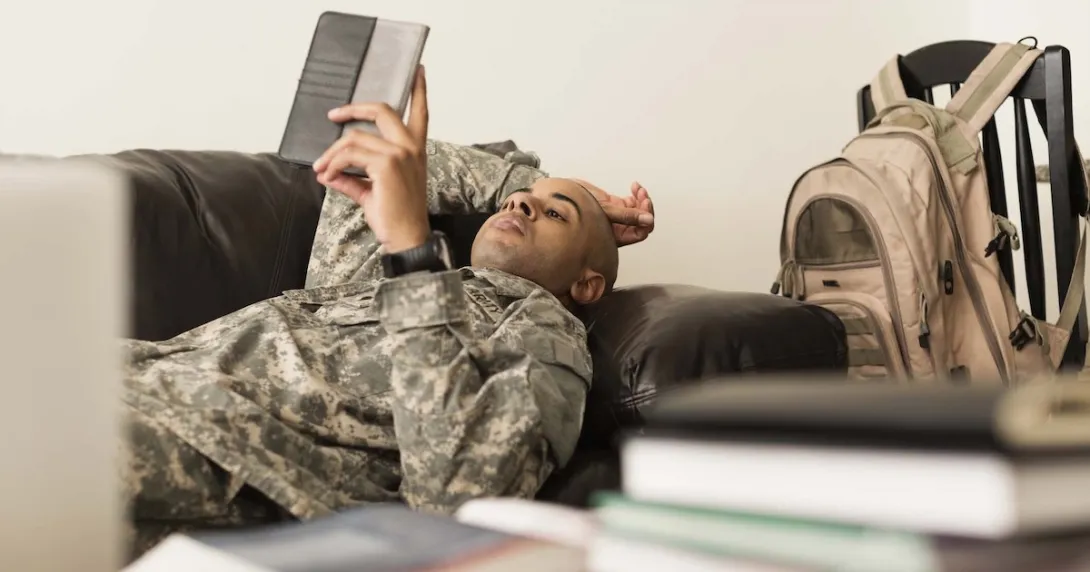Soldier using digital tablet on sofa near books