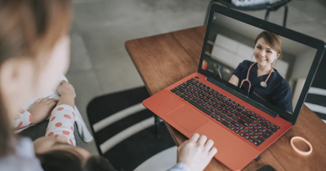 Person sitting down looking at a computer on a coffee table, talking to a healthcare provider