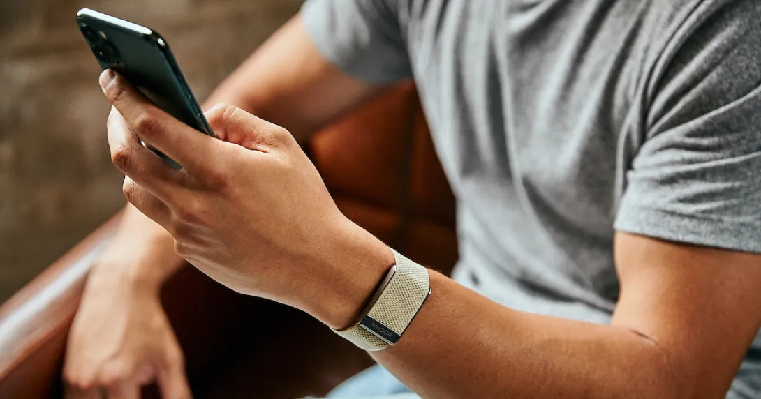 A close up of a man wearing the WHOOP 4.0 on his wrist while using a smartphone
