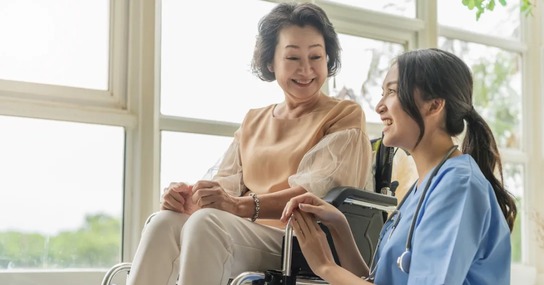 A caregiver kneeling beside a senior patient on a wheelchair