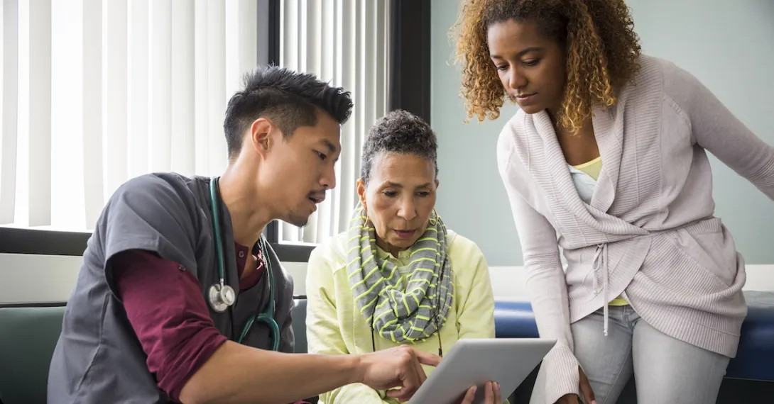 A doctor using a tablet while talking to a patient and her family member.