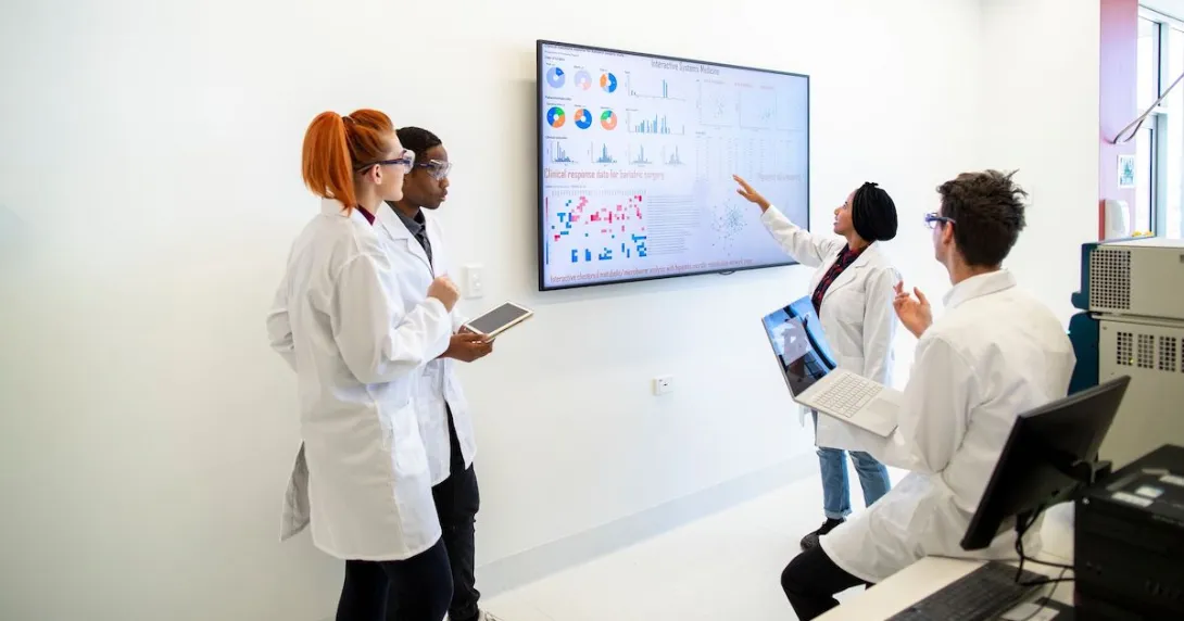 A group of providers or researchers looking at a data dashboard on a large TV on a wall