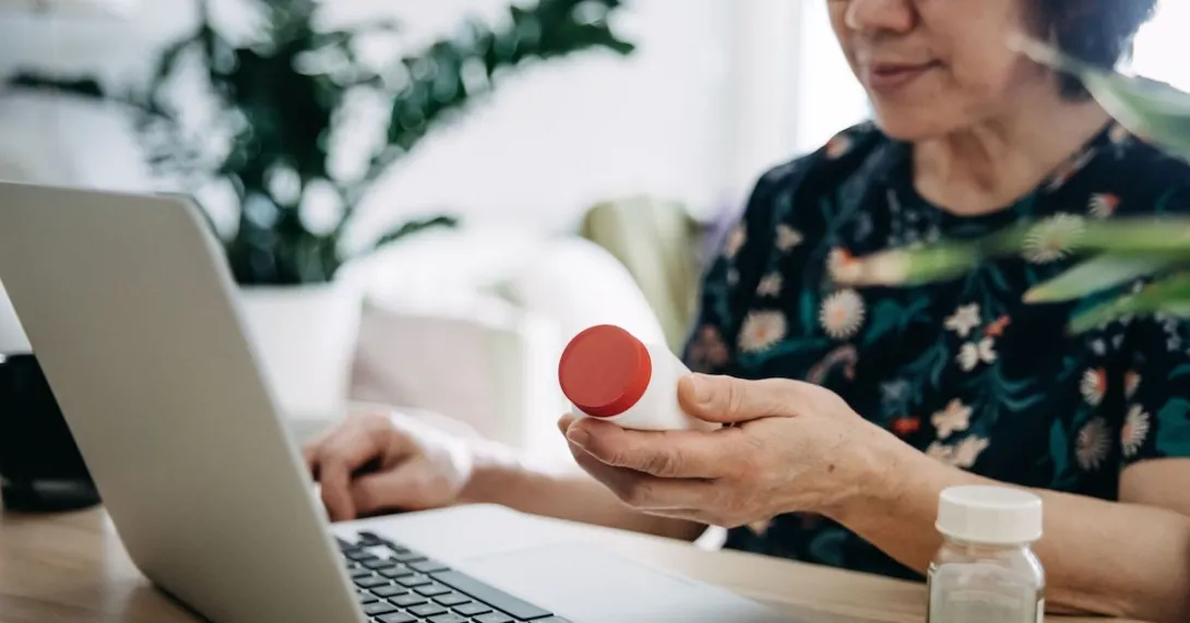 A close up of a woman holding a prescription bottle while using a laptop