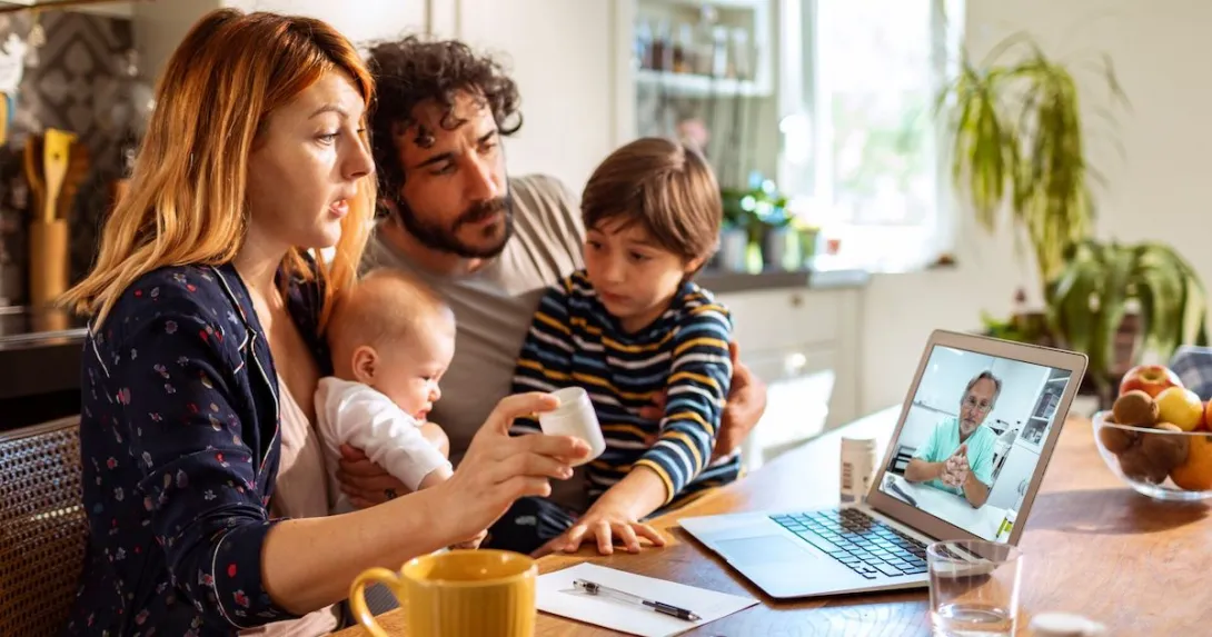 Parents with two young children talk to a provider through a video call on their laptop.