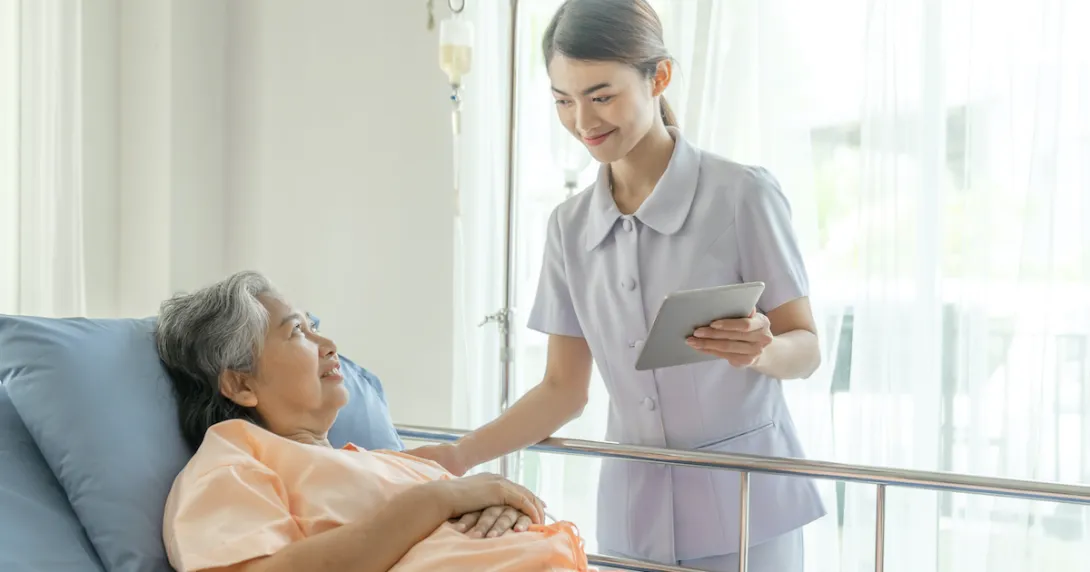 A nurse holding a tablet is taking care of an elderly patient in bed