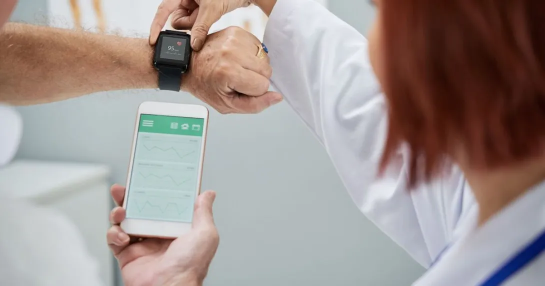 Doctor showing senior patient how to synchronize health app in smartphone and smartwatch