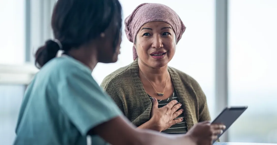Healthcare provider sitting next to a patient with a scarf on their head while looking at a tablet