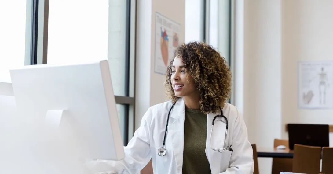 Healthcare provider with a lab coat on sitting at a desk and looking at a computer