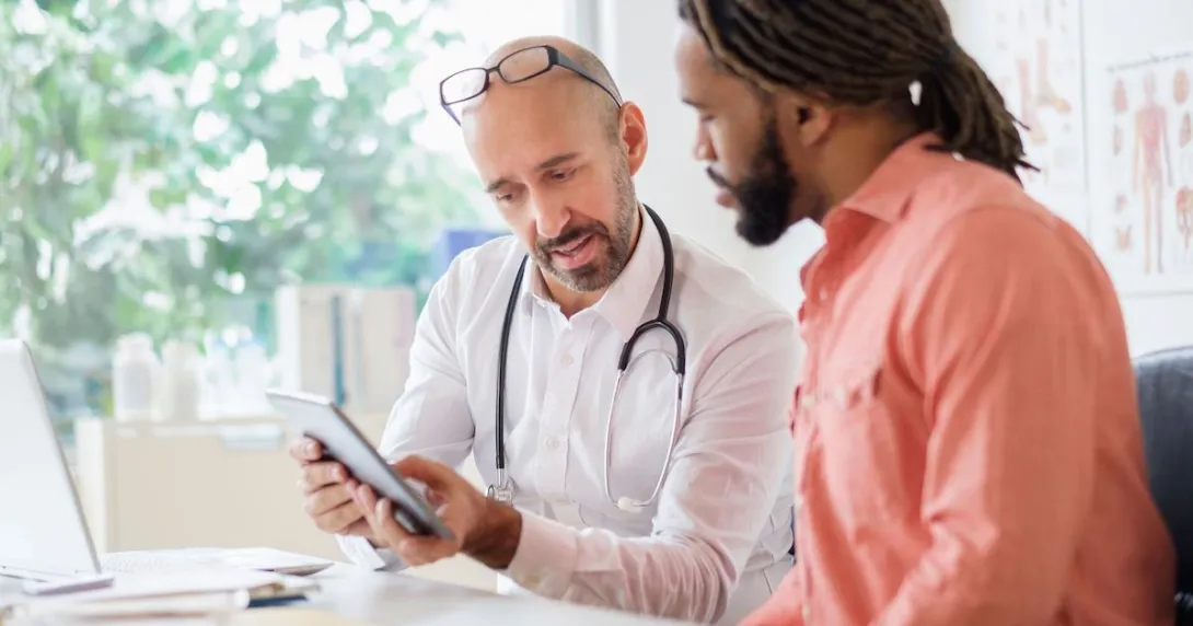 Healthcare provider and patient with an orange shirt sitting at a desk and looking at a tablet