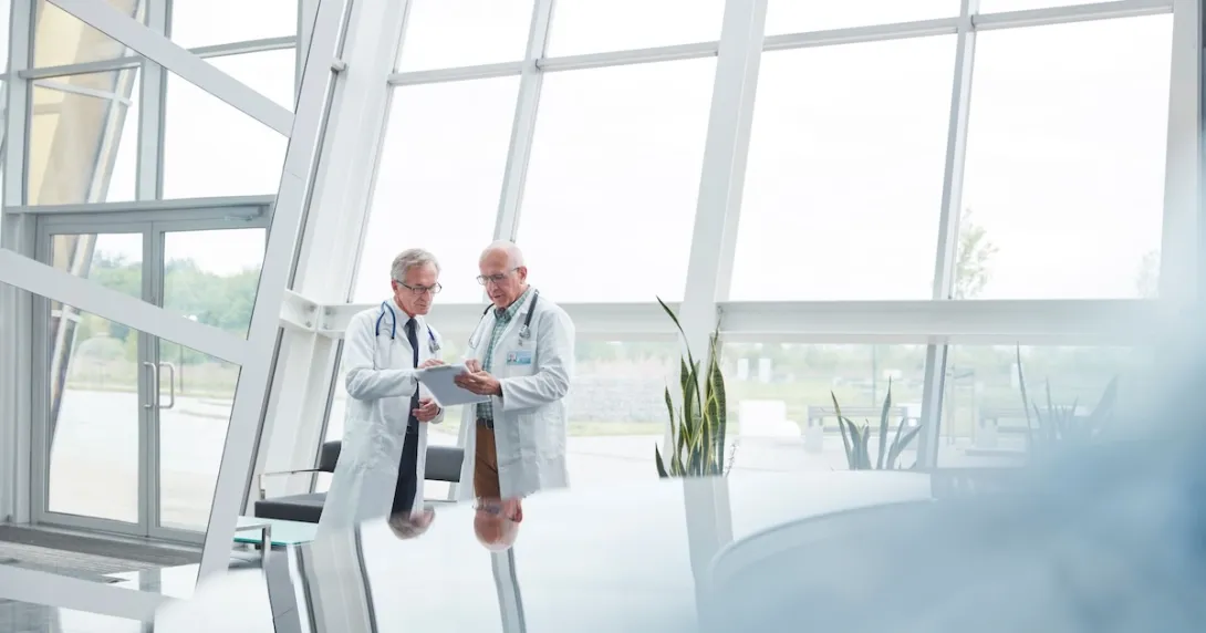 Two healthcare professionals standing in a large room with windows