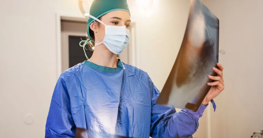Healthcare provider in scrubs wearing a mask and looking at a large diagnostic image