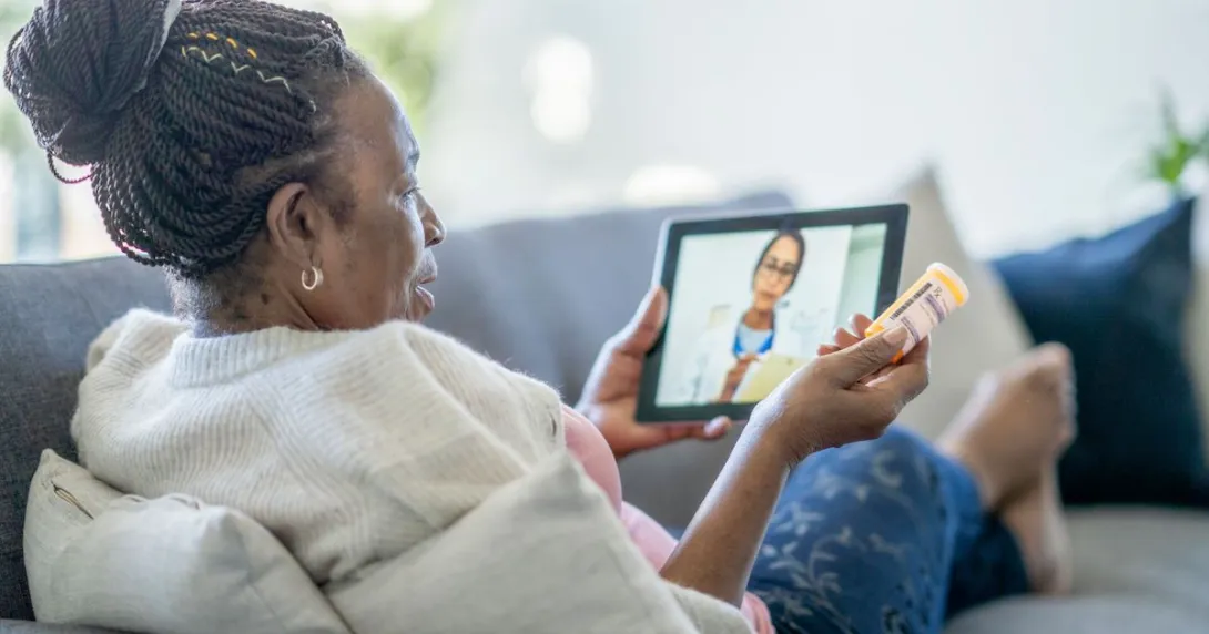 Person sitting on a couch holding a tablet on their lap with a healthcare professional on the screen