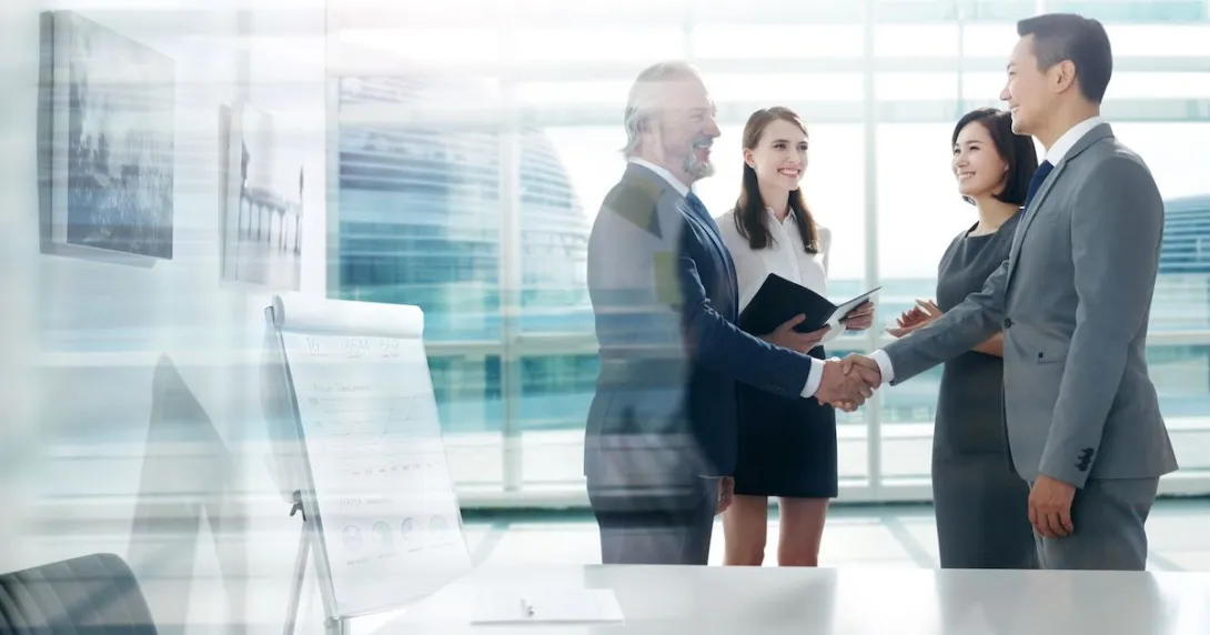 Four people standing in front of a large window with two of them shaking hands