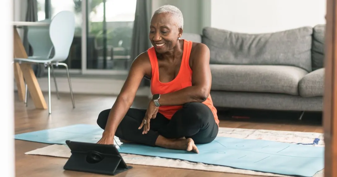 A person using a tablet while sitting on a yoga mat and preparing to exercise
